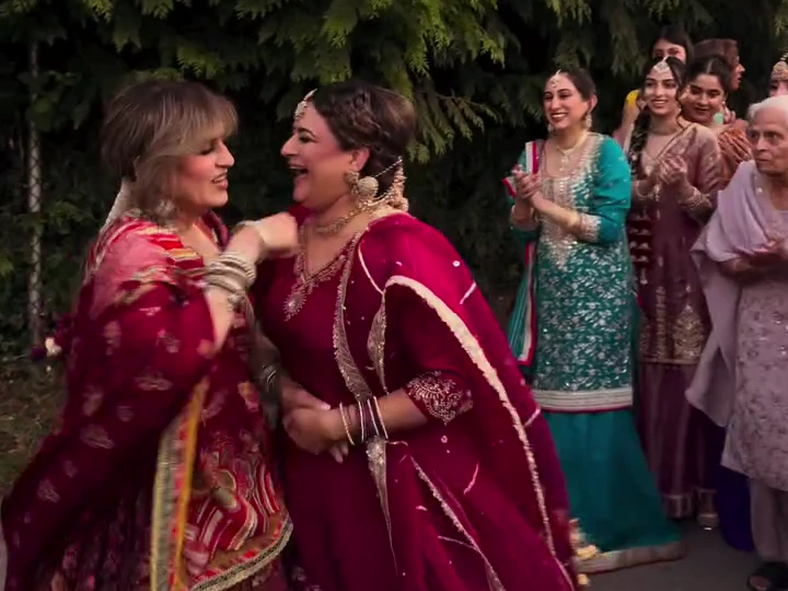 Two women laughing and dancing outdoors as wedding guests clap along