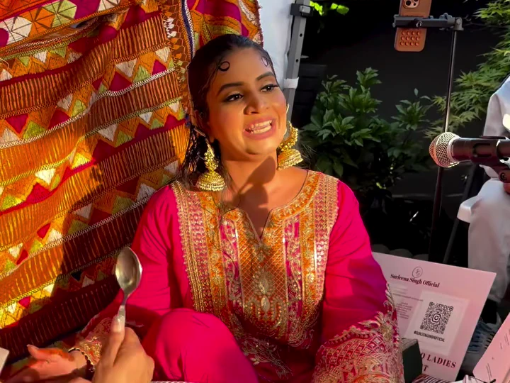 Surleena smiling in a bright pink outfit beside a microphone and colourful phulkari fabric